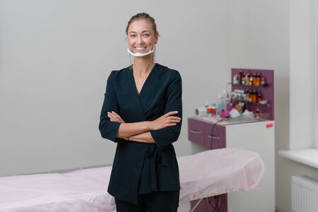 Cosmetology cabinet. Beautician stands in mask and smiles. Preparation for the procedure of permanent eyebrow or lips makeup. Cosmetologist in working space.の写真素材
