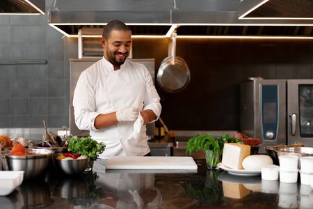 young attractive male cook blows up his protective glove jokes and has fun in the professional kitchen Handsome black chef dressed in white uniform on workplaceの写真素材