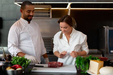 Handsome young African chef is cooking together with Caucasian girlfriend in the kitchen A cook teaches a girl how to cook. Man and woman cooking in professional kitchen. interracial relationshipの写真素材