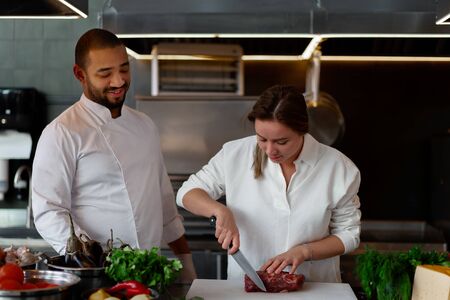 Handsome young African chef is cooking together with Caucasian girlfriend in the kitchen A cook teaches a girl how to cook. Man and woman cooking in professional kitchen. interracial relationshipの写真素材