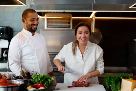Handsome young African chef is cooking together with Caucasian girlfriend in the kitchen A cook teaches a girl how to cook. Man and woman cooking in professional kitchen. interracial relationshipの写真素材