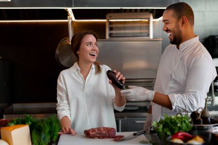 Handsome young African chef is cooking together with Caucasian girlfriend in the kitchen A cook teaches a girl how to cook. Man and woman cooking in professional kitchen. interracial relationshipの写真素材