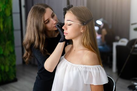 Young beautician caucasian girl holds model eyebrow correction Beautician at work is the workplace of an eyebrow specialist. Eyebrow correction and dyeing procedure. Beauty industry. Lifestyleの写真素材
