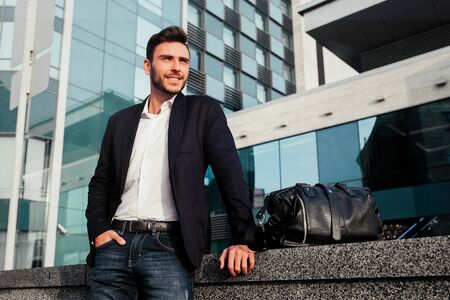 Men's fashion. A young male businessman in a trendy suit and a white shirt with a big black handbag comes out from a fashionable clothing store. Outdoor.の写真素材