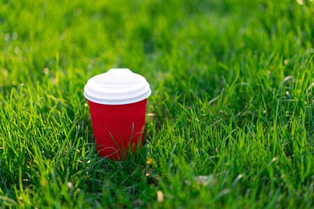 A red disposable cardboard cup with hot tea stands in fresh green grass. morning fresh conceptの写真素材
