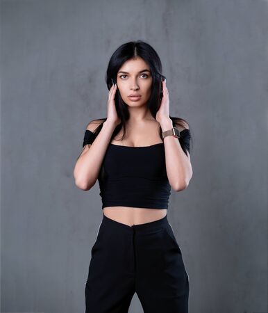 young caucasian brunette girl is standing in the studio on a dark background with something restless holds hands near her head Worried womanの写真素材