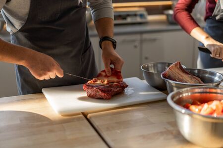 Chef in gray apron cuts meat on a plastic board. Closeup photo of the culinary process. Unrecognizable man is cooking meat in the kitchen.の写真素材