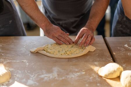 Culinary master class. Closeup of male hands preparing khachapuri. Traditional georgian cheese bread. Georgian food. Unrecognizable male cook preparing dishes from the dough. Hands close upの写真素材