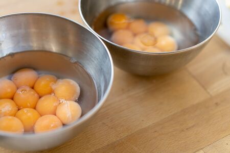 Two stainless steel bowls filled with many cracked eggs with whole yolks, in the wooden table. Close up.の写真素材