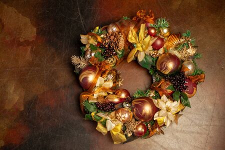 Christmas wreath on brown background with copyspace. Wreath decorated with balls and bows of gold and brown, with green leaves. Luxury New Year decorの写真素材