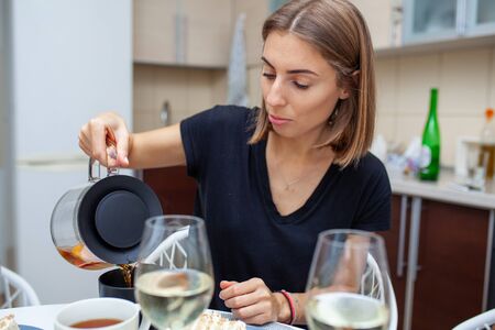 Closeup of male hands pouring tea into a cup. On the side on the table is a glass of wine and a piece of cake. Domestic life.の写真素材