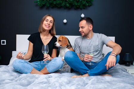 Young couple sitting on a bed in the bedroom, hugging. Near them is their dog. Domestic animal Beagleの写真素材