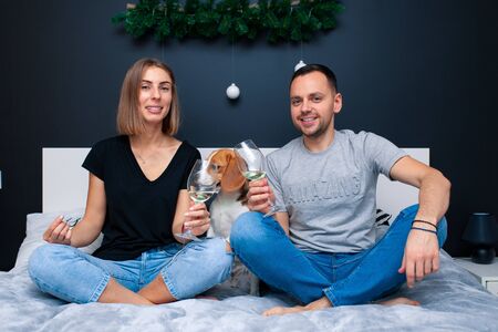 Young couple sitting on a bed in the bedroom, hugging. Near them is their dog. Domestic animal Beagleの写真素材