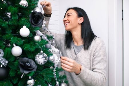A young woman decorate the Christmas tree, preparing for the New Year's celebration. Female decorate a Christmas tree. Beautiful girl are smiling and have fun during the Christmas holidays.の写真素材