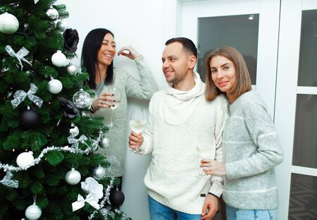 Two young women decorate the Christmas tree, preparing for the New Year's celebration. Friends decorate a Christmas tree. Beautiful girls are smiling and have fun during the Christmas holidays.の写真素材