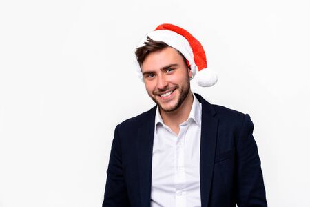 Young handsome caucasian guy in business suit and Santa hats stands on white background in studio teeth smilie. Close up portrait business person with Christmas mood Holiday bannerの写真素材