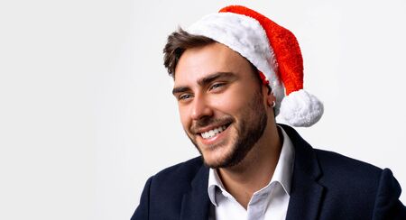 Young handsome caucasian guy in business suit and Santa hats stands on white background in studio teeth smilie. Close up portrait business person with Christmas mood Holiday bannerの写真素材