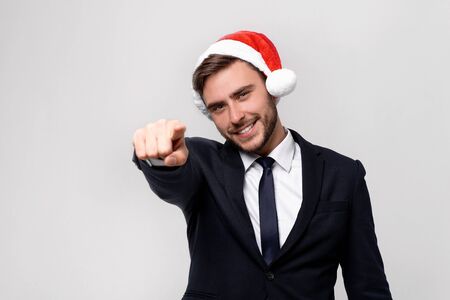 Young handsome caucasian guy in business suit and Santa hats on white background in studio smilie and showing Finger to the camera. Close up portrait business person with Christmas mood Holiday bannerの写真素材
