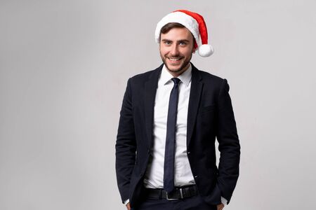 Young handsome caucasian guy in business suit and Santa hats stands on white background in studio teeth smilie. Close up portrait business person with Christmas mood Holiday bannerの写真素材