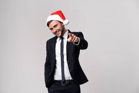 Young handsome caucasian guy in business suit and Santa hats on white background in studio smilie and showing Finger to the camera. Close up portrait business person with Christmas mood Holiday bannerの写真素材