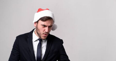 Young handsome caucasian guy in business suit and Santa hats stands on white background in studio Surprisedly look aside. Close up portrait business person with Christmas mood Holiday bannerの写真素材