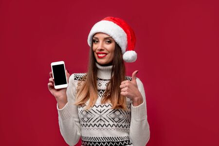 Close up portrait beautiful caucasian woman in red Santa hat on red studio background. Christmas New Year holiday concept. Cute girl teeth smiling positive emotions with free copy spaceの写真素材