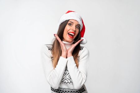Close up portrait beautiful caucasian woman in red Santa hat on white studio background. Christmas New Year holiday concept. Cute girl teeth smiling positive emotions with free copy spaceの写真素材
