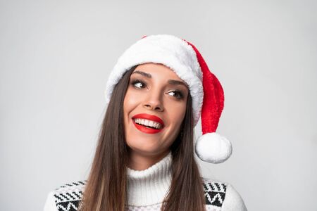 Close up portrait beautiful caucasian woman in red Santa hat on white studio background. Christmas New Year holiday concept. Cute girl teeth smiling positive emotions with free copy spaceの写真素材