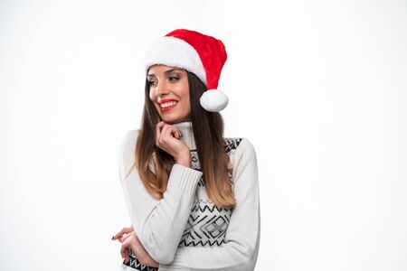 Close up portrait beautiful caucasian woman in red Santa hat on white studio background. Christmas New Year holiday concept. Cute girl hand on collar teeth smiling positive emotions with free spaceの写真素材