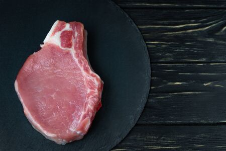 Top view of one pieces raw pork chop steaks on a black stone cutting board. Wooden table.の写真素材