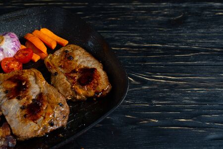 Juicy piece of fried meat in a pan that stands on a black wooden table background with copy spaceの写真素材