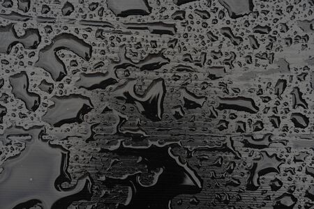 Rain water drops on black surface. Liquid on dark wooden background. Abstract concept with dark mood.の写真素材
