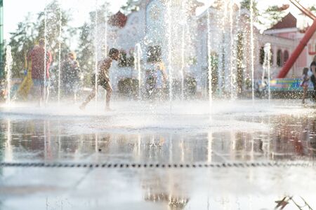 Unrecognizable Happy kids have fun playing in city dry water fountain on hot summer day. Parents with their children. Active family leisure. Summertime conceptの写真素材