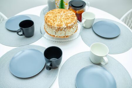White biscuit cake cut on a stand on a serving table. Around the cake lay out plates with cups and tea.の写真素材