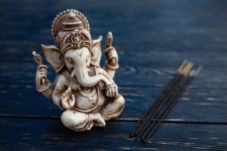 Hindu god Ganesh on black wooden background. Statue on table with sandalwood stick close up with copy space for textの写真素材