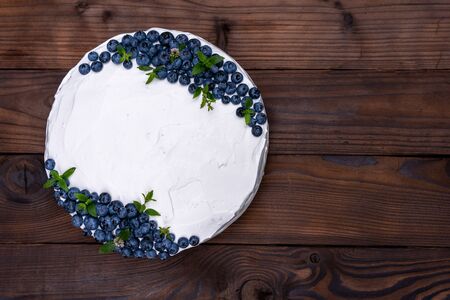 Appetizing cheesecake biscuit pillow decorated white cream blueberries and mint stands on wooden rustic table. Sweet cake with piece on plateの写真素材