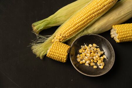 Corn cob with green leaves lies on table. black color background. Copy space for text.の写真素材
