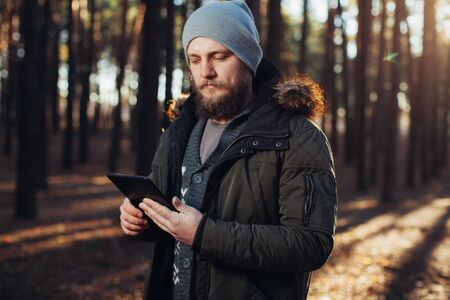 Portrait of adult man walking in the pine forest with digital tablet. Modern technology help navigateの写真素材