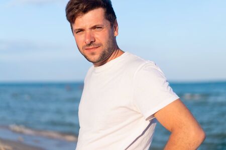 Caucasian man standing on the sea beach dressing white shirt looking at the camera