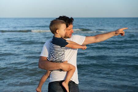 Young Caucasian dad with little son walk warm summer day along the sea coast. Summer family vacation concept. Friendship father and son. Happy childhood on the beach with parent. free space for textの写真素材