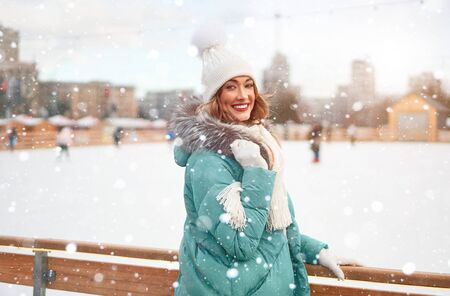 Beautiful lovely middle-aged girl curly hair warm winter jackets white knitted hat glove stands ice rink background Town Square Christmas mood lifestyle Happy holiday woman  snowy day Winter leisure の写真素材