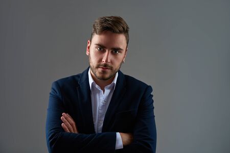 Close up portrait young man businessman. Caucasian guy business suit studio gray background. Modern business person folded his arms over his chest Portrait of charming successful young entrepreneurの写真素材