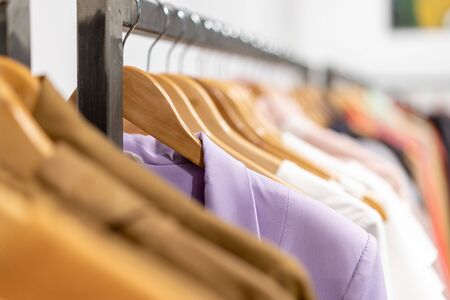 Multi colored clothing shirts hang on hangers in a shop background. A variety of clothes  hanging in...