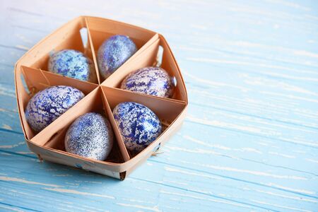 Blue chicken eggs lie in round wooden basket which stands on a blue wooden table. Easter background. Seasonal holiday flat lay with free space for text. Classic blue color of the year 2020の写真素材