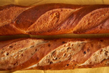 two crispy french baguettes lie yellow cloth napkin wooden table background baguettes in assortment with sesame seeds Classic french national pastries Copy space Concept for menu or advertisingの写真素材