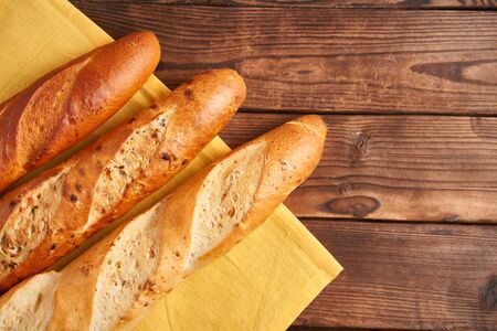 Three crispy french baguettes lie yellow cloth napkin wooden table background baguettes in assortment with sesame seeds Classic french national pastries Copy space Concept for menu or advertisingの写真素材