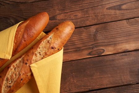 two crispy french baguettes lie yellow cloth napkin wooden table background baguettes in assortment with sesame seeds Classic french national pastries Copy space Concept for menu or advertisingの写真素材