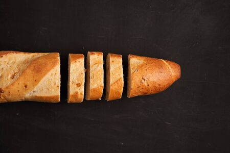 one sliced crispy french baguettes lie dark black table background sesame seeds Classic french national pastries Copy space Concept for menu or advertisingの写真素材
