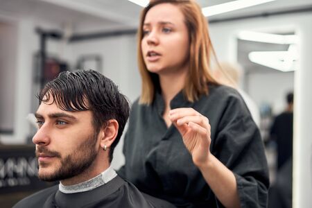 Stylish man sitting barber shop Hairstylist Hairdresser Woman cutting his hair Portrait handsome happy young bearded caucasian guy getting trendy haircut Attractive barber girl working serving client の写真素材