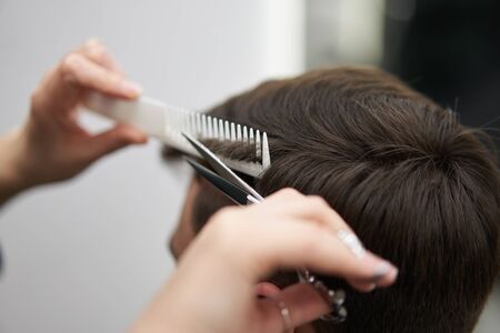 Beautiful caucasian woman hairdresser doing hairstyle to client. Close up portrait female barber with hairdressing tools at work. hair cutting process  Hairstyling in modern barbershop. Professionalの写真素材